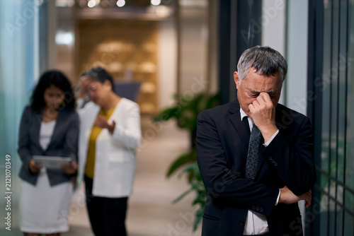 Stressed Senior Asian Businessman with Headache in Office Corridor, Disappointed Male Executive Suffering from Burnout or Business Failure Concept