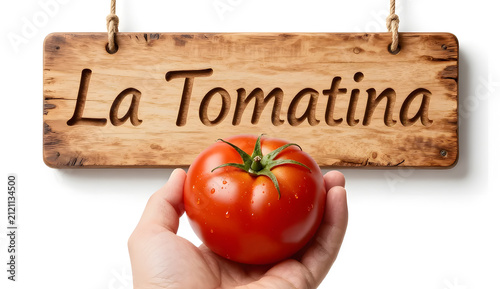 A hand gently squeezing a ripe tomato with subtle juice droplets, paired with a rustic wooden-style “La Tomatina” sign, premium studio lighting, white backdrop, lively festive spirit.