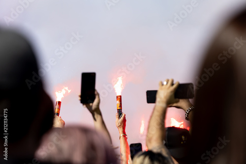 Fotografie Hands hold burning torches and smartphones aloft