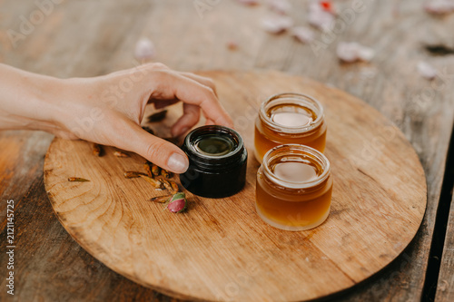 Foto Hand reaching toward natural skincare jars on rustic wooden board with amber bal