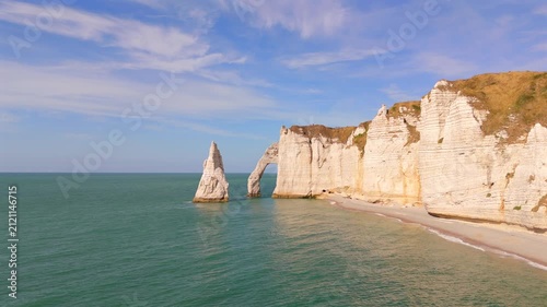 A low aerial shot captures a limestone arch and rock spire along the coast near Etretat, France.