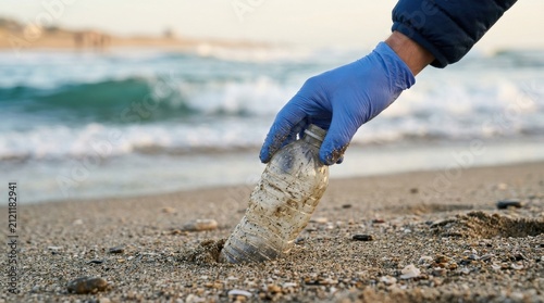 Hand blue nitrile glove picking discarded plastic bottle sandy beach ocean shore