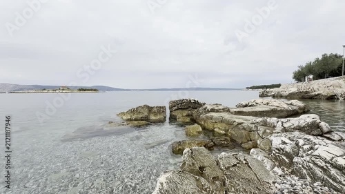 Crystal clear Adriatic Sea water gently washing over a rocky shoreline in Novi Vinodolski, Croatia. Close-up of transparent water revealing underwater stones on a sunny summer day.