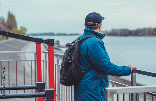 Thoughtful senior man aged 50s 60s in blue jacket and cap standing alone outdoors looking into distance, psychological mental health concept of loneliness and reflection