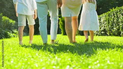 Barefoot family walking on grass holding hands. Summer vacation. Big happy family. Motherhood childhood concept. Parents and children. Healthy young family at sunny day. 4K, UHD