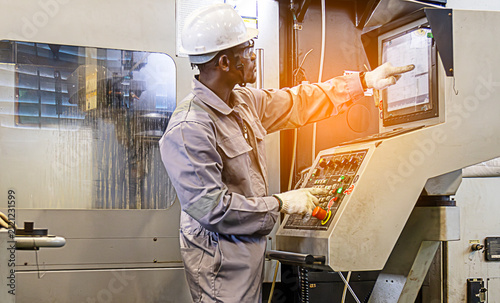 African American engineer operating industrial machinery on a factory control panelFactory worker in hard hat and safety glasses operating CNC machine equipmentIndustrial technician pressing buttons.