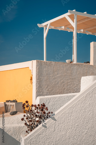 Minimalist cycladic architecture featuring a pergola, white steps, and a vibrant yellow wall under blue sky