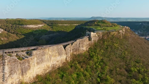 Panoramic aerial view of Ovech Fortress standing on a high rock plateau in Provadia, Bulgaria, with a long wooden bridge connecting the medieval cliff walls