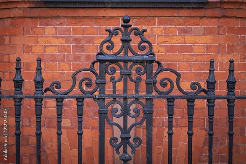 Black, ornate wrought iron fence in front of a brown-red brick wall, Chelsea, London, England, Great Britain