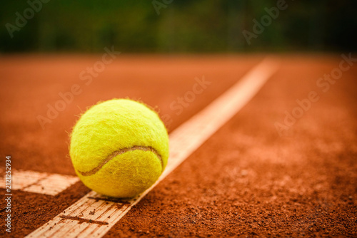 Gelber Tennisball direkt auf der weißen Spielfeldlinie eines roten Sandplatzes mit geringer Tiefenschärfe und Freiraum für Text.