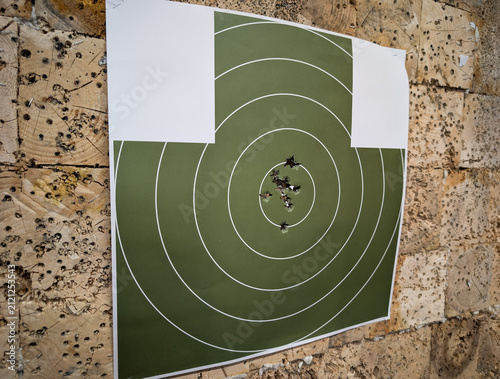 Foto Angle view of paper shooting target with 45 ACP pistol bullet holes grouped in bullseye on wooden backstop at indoor firing range