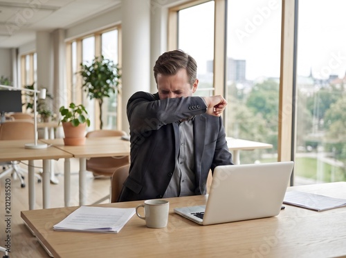 Man sneezing into elbow in modern office
