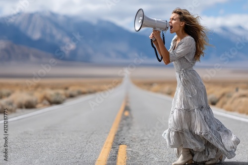 Woman in a flowing dress passionately speaks into a megaphone on a deserted highway