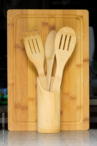 A set of natural bamboo kitchen tools including a cutting board and utensils in a holder, ready for cooking and preparing meals. Eco-friendly and rustic.