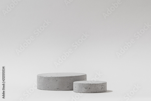 A pair of round concrete cylinder pedestals of different heights centered in frame on a light gray background, showing detailed stone texture, designed for product placement and advertising mockups.