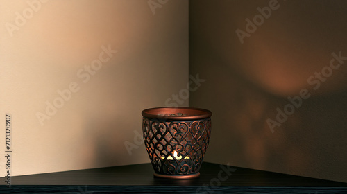 Beautiful decorative candle holder with intricate patterns and burning tealight candle placed on a corner shelf, creating warm ambient light and soothing atmosphere