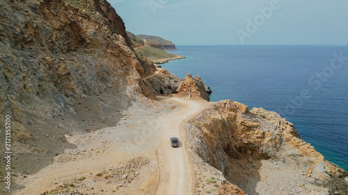 Fotografía Drone aerial view of car driving along dirt coastal road next to sea cliffs towa