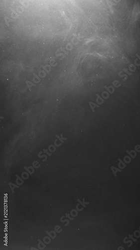 Dark, swirling smoke drifts and flows downward against a black background, illuminated from above by a soft, diffused light that highlights the particles within.