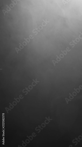 Dark smoke swirls and drifts upward in a vertical space, illuminated from above against a black background.