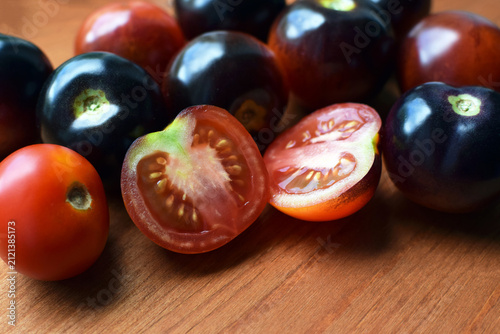 Black and red tomatoes, whole and cut, lie on a wooden board.