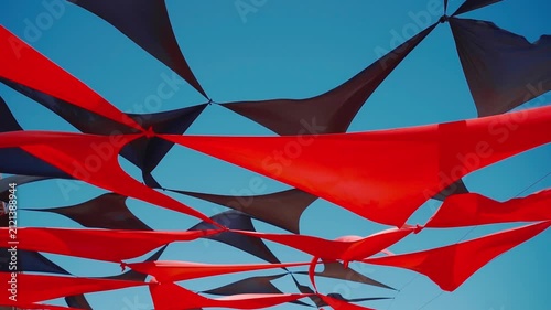abstract view of red and black triangle shaped cloth decoration waving by wind on blue sky background. summer sea camp or beach club decoration, vibrant colors