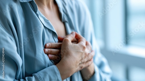 A close-up shot of a person holding their chest with both hands, appearing to experience discomfort or pain. The blue shirt is softly lit, creating a somber mood.