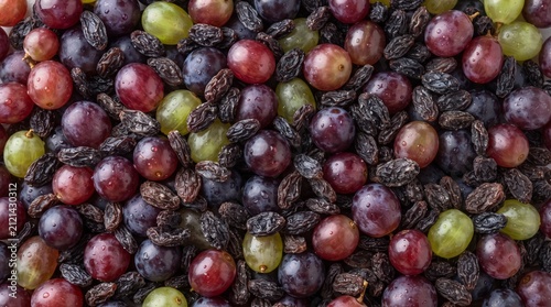 A Colorful Medley of Grapes and Raisins: A vibrant and textured close-up shot showcases a rich assortment of fresh red, green, and purple grapes mingled with dark, sweet raisins.
