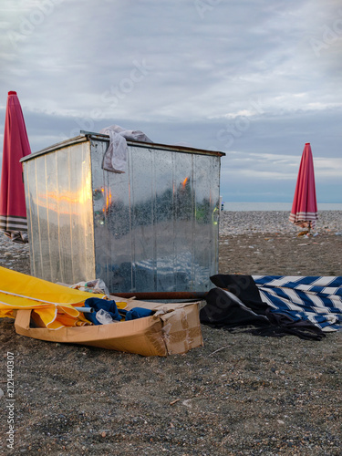 Vertical shot of an old metal storage box with a folded beach umbrella and discarded cardboard left on a shore at dusk.