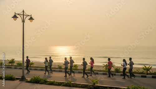 Group of joggers running along the coastal road in Visakhapatnam during a serene morning atmosphere on the beach for health and wellness concept in golden sunrise light