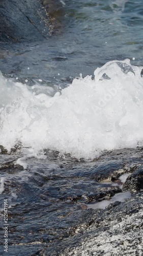 Vertical ocean waves crashing on rocks. Slowmotion sea water splashing against stone shore.