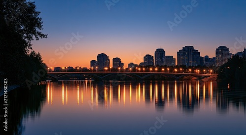 City skyline glows reflecting on calm river at twilight with a bridge