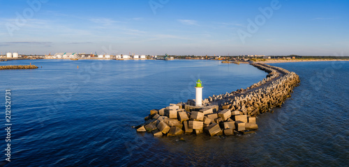 Картината върху платно A wide aerial view shows the curving stone breakwater to Ventspils, Latvia, with a white lighthouse with a green top, port structures, tetrapods, and calm daylight