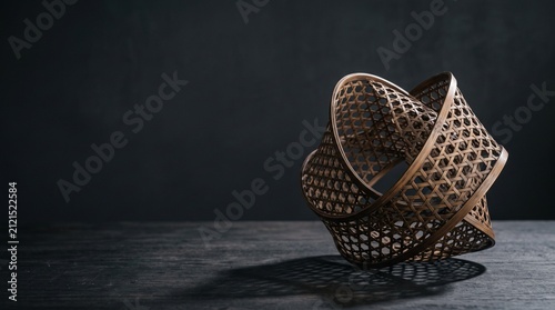Abstract contemporary Japanese bamboo weaving art sculpture on dark wooden table with intricate shadow