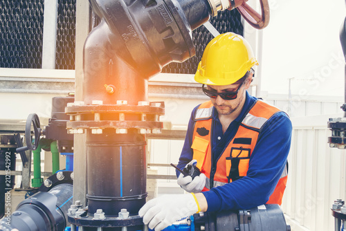 Fotografie Industrial engineer with radio communicator inspecting factory cooling tower pipelineMaintenance technician in a hard hat and safety vest checking water valve pipesCaucasian supervisor monitoring