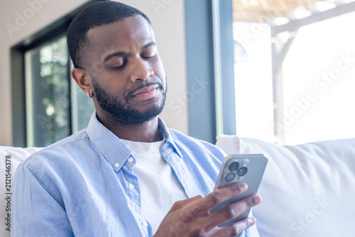 Photography Young man sitting indoors, intently reading content on his smartphone with a ske
