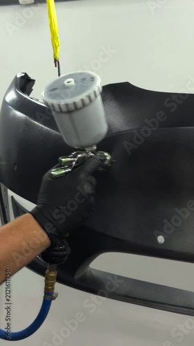 Professional auto body painter applying primer to a car bumper with a spray gun