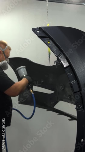 Professional auto body painter applying finish to car bumper with spray gun