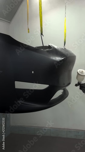 Automotive bumper receiving a professional spray paint application in a clean booth