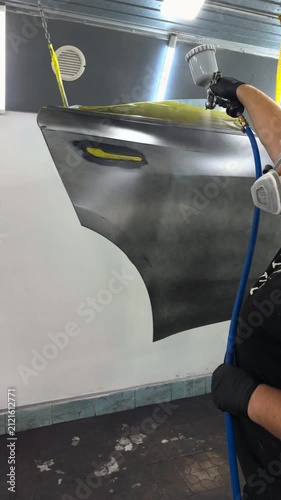 Professional auto body painter applying primer to a car panel in a spray booth