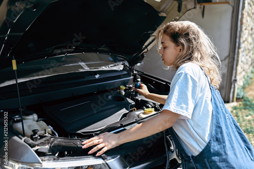 Woman checks car engine in garage during daytime