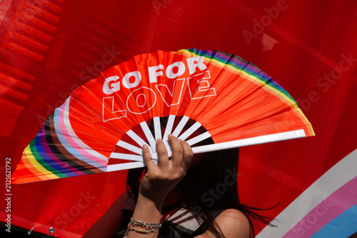 Participant is hiding from the sun with rainbow colored fan and sign 