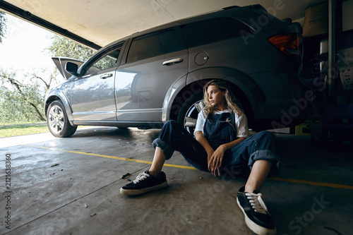 Girl sits on garage floor next to vehicle in the afternoon