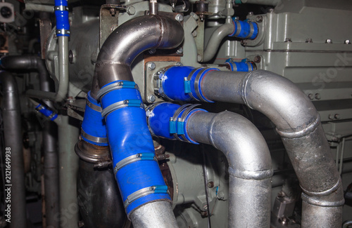 Connecting steel pipes with blue silicone hoses and metal clamps on marine diesel generator engine inside room