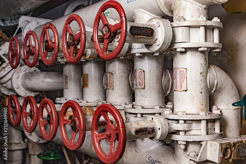 Industrial pipeline system with rows of red gate valves and steel white pipes in machinery engine room