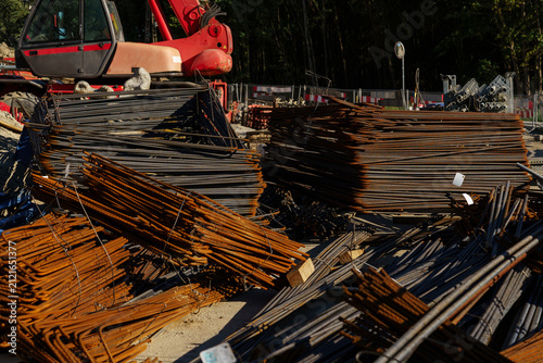 Photography Stacks of rusted rebar piled on the ground at a sunny construction site, with a