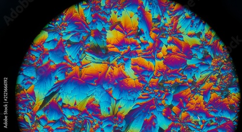 Microscope reveals a vibrant circular pattern of crystalline structures displaying intense neon rainbow colors.