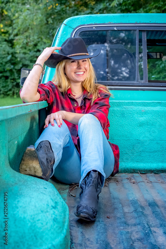 Golden Hour Country Lifestyle Portrait of a Beautiful Young Cowgirl Leaning Against a Modern Pickup Truck in Warm Evening Sunlight