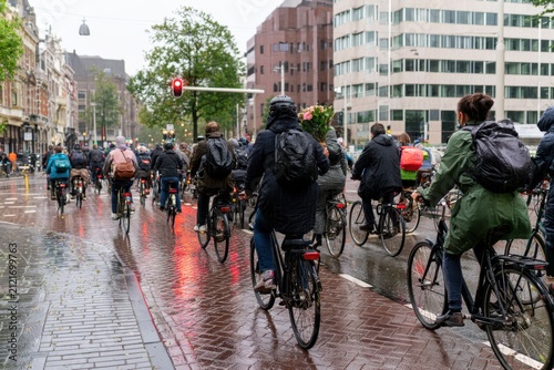 a group of people ride bicycles on a wet city street on an overcast day