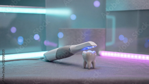 Intraoral scanner tool emits blue light onto a small dental model in a clinical research laboratory.