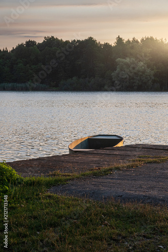 Obraz na plátně Metal rowboat anchored by a concrete pier on a fish breeding pond at sunset